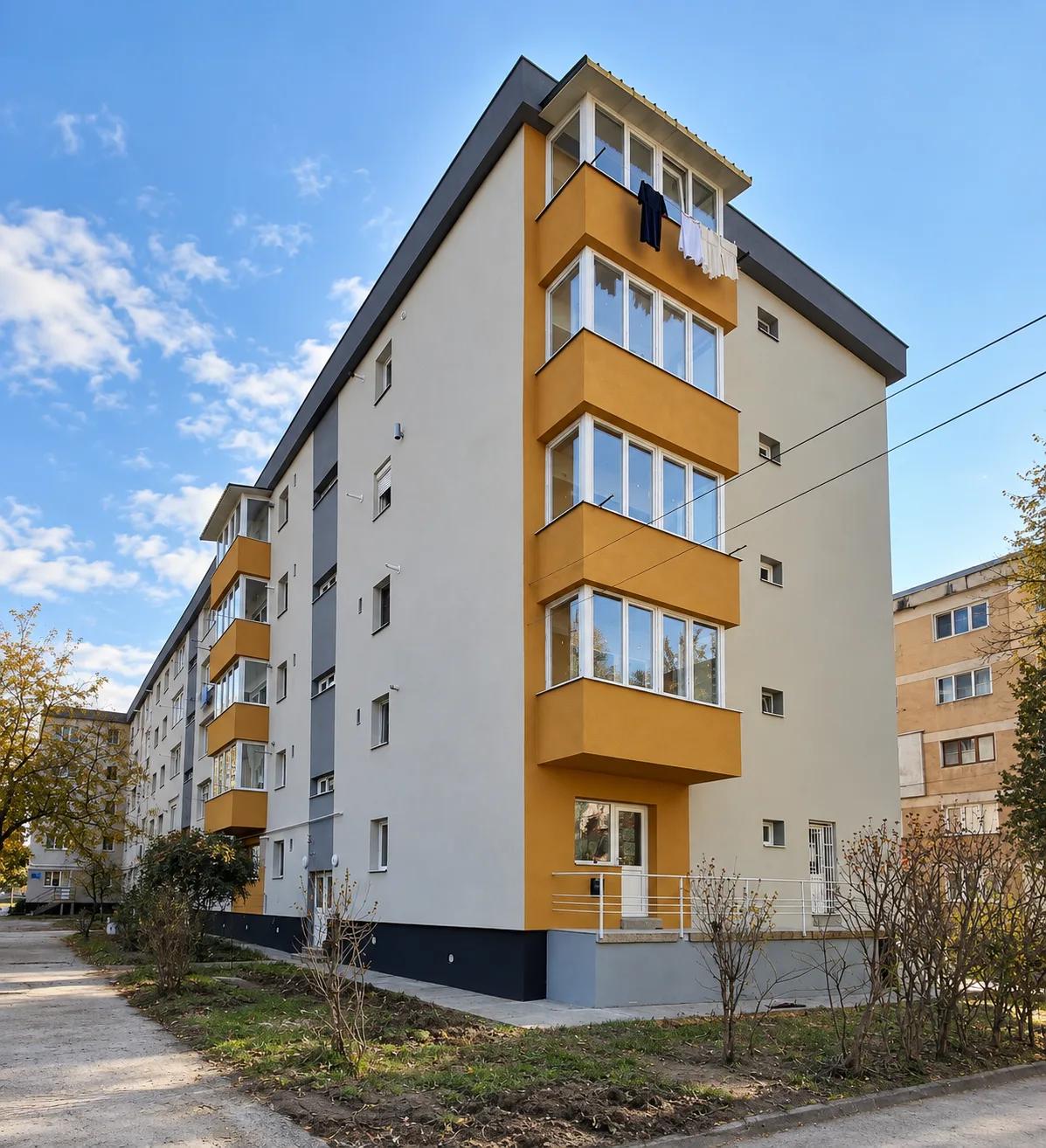 Bloc de locuințe P+4 reabilitat, cu fațadă gri deschis și balcoane închise, finisate în galben